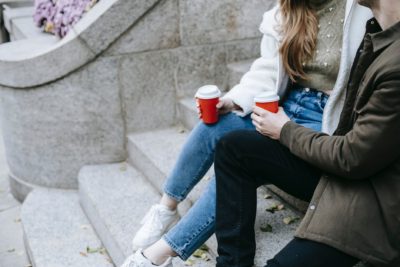 young man and woman sitting on stairs on street and having hot drinks